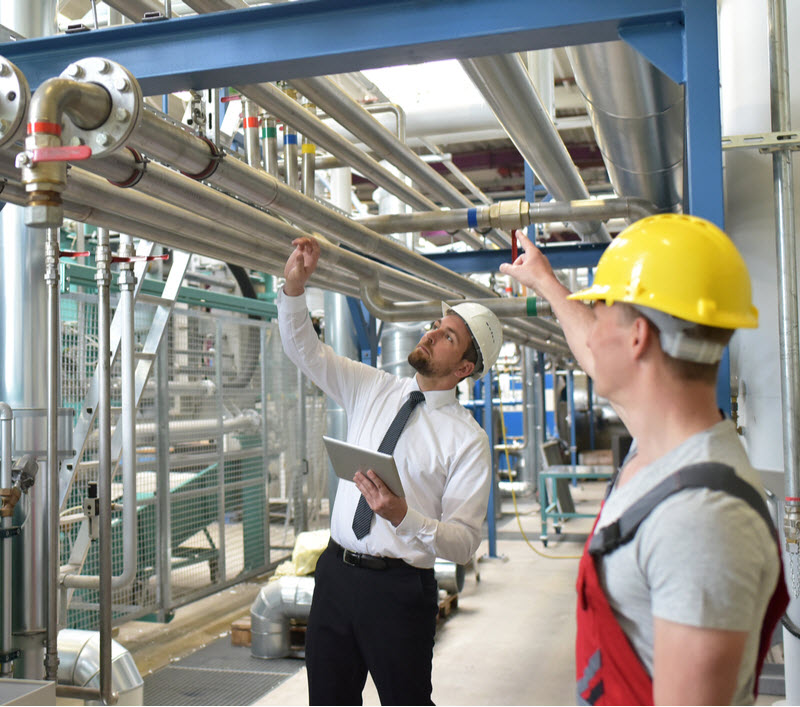 Businessman wearing hard hat with worker meeting in a factory