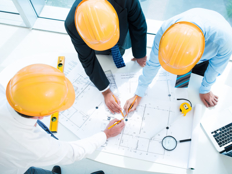 Engineers wearing hard hats discussing the plan of the construction project