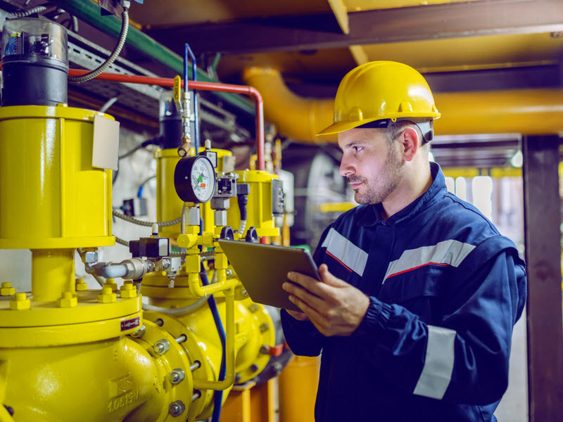 worker in protective uniform and with hardhat using tablet for checking temperature in pipes