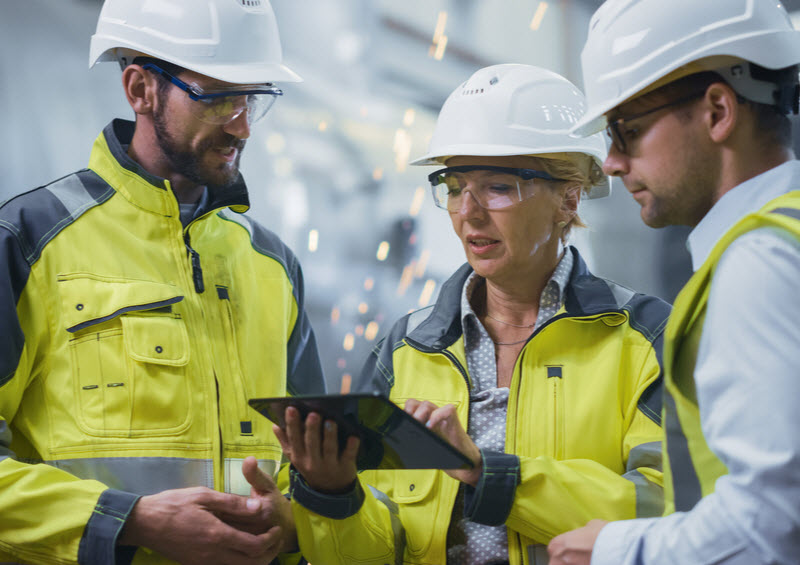 Three engineers wearing hard hat discussing while using a tablet inside the factory