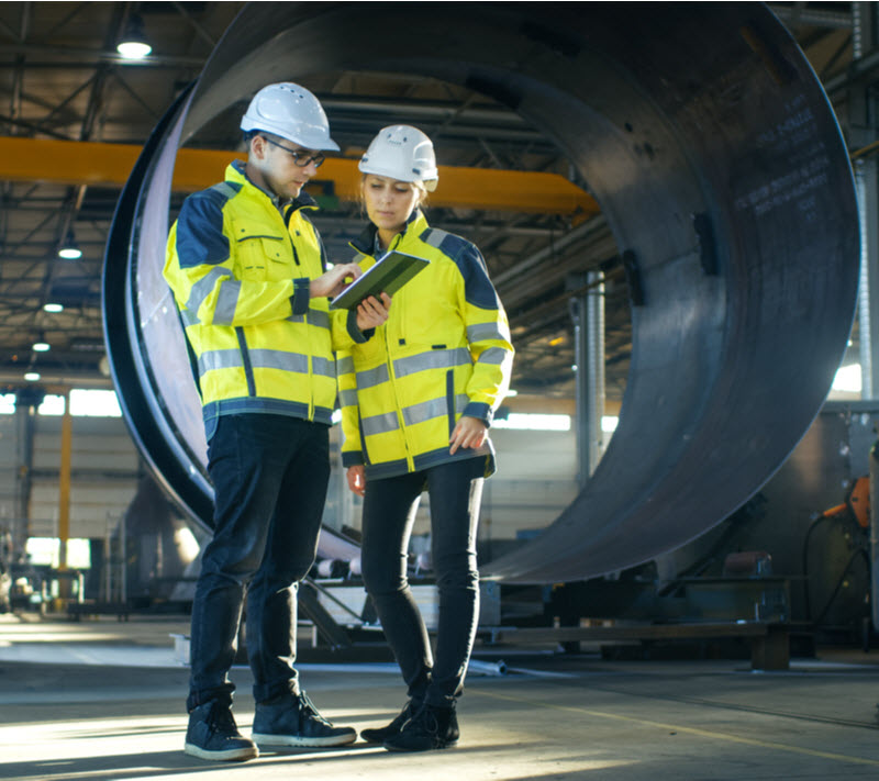 Male and Female Industrial Engineers in Hard Hats Discuss New Project while Using Tablet Computer