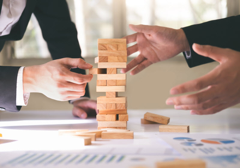 Businessmen playing stack and fall blocks with financial report at the table